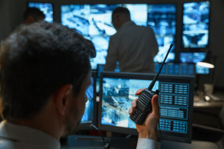 A male security guard in the security room keeps order with the help of modern technologies. The security service monitors display all the information from the surveillance cameras.